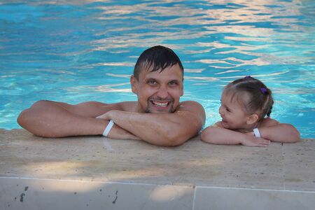 a man with a child swimming in the pool. Dad with daughter in the waterの写真素材