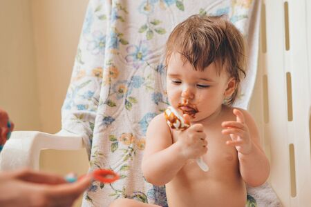 portrait of a child who eats baby food from a spoon. Grimy face in foodの写真素材