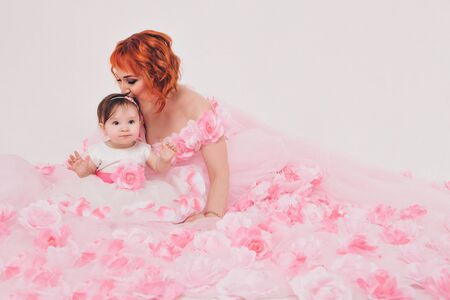 the child in the arms of his mother in a pink dress of flowers. A woman with a child in her arms on a white background, isolatedの写真素材