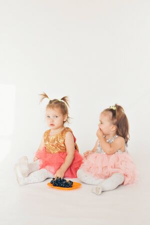 two little girls eating grapes sitting on the floor on a white backgroundの写真素材