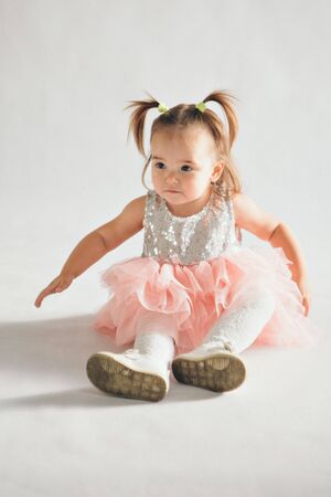 a little girl in a dress sits on the floor on a white background. Child promotes children's clothesの写真素材
