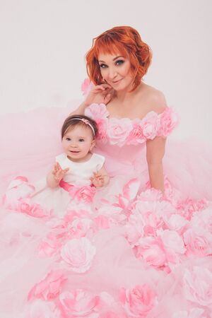 the child in the arms of his mother in a pink dress of flowers. A woman with a child in her arms on a white background, isolatedの写真素材