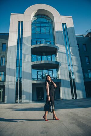 portrait of a beautiful girl in a black dress and red shoes on the background of the business centerの写真素材
