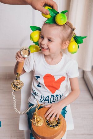 a little girl with a wreath of lemons on her head talking on an old phoneの写真素材