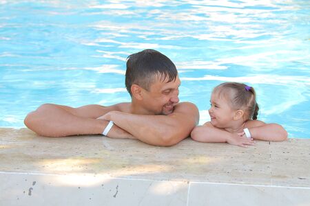 a man with a child swimming in the pool. Dad with daughter in the waterの写真素材