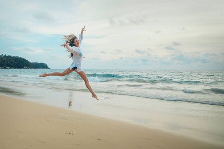 woman jumping happy in the beach with a blue sky and sea in the backgroundの写真素材