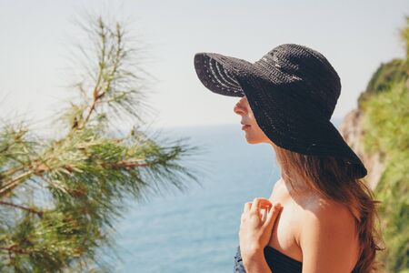 portrait of a tourist with long hair in black hat against the rocks and the sea. woman in travelの写真素材