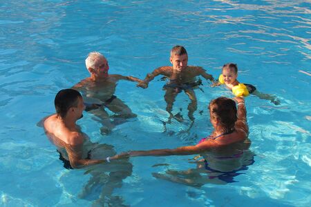 The concept of sports, recreation, healthy lifestyle - 5 people swim in the pool forming a circle. People in the water holding handsの写真素材