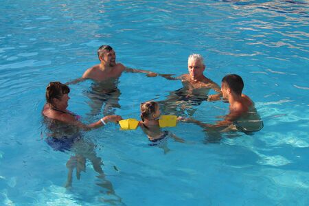 The concept of sports, recreation, healthy lifestyle - 5 people swim in the pool forming a circle. People in the water holding handsの写真素材