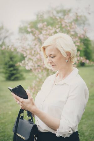 entrepreneur talking on the phone in the Park. Blonde hair Bob works outside. businesswoman with smartphoneの写真素材