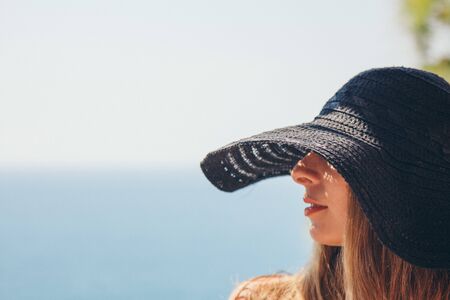 portrait of a tourist with long hair in black hat against the rocks and the sea. woman in travelの写真素材