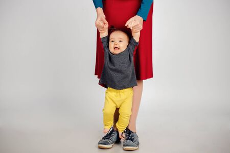 Cute baby learning to walk and make his first steps. mom is holding his hand. child's feet close up, copy spaceの写真素材