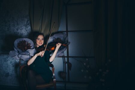 the concept of music education, the fashion Industry-a beautiful girl playing the violin among the big artificial flowers at dusk. Beauty in a dress among creative sceneryの写真素材