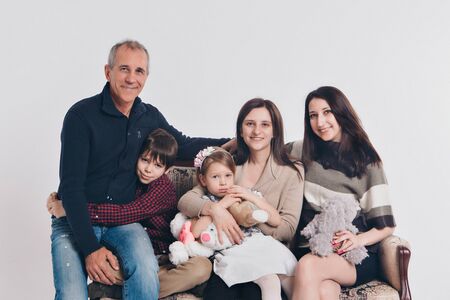 concept of happy childhood, family, love - group of people on a white background: adults and children with toys sitting on the same couchの写真素材