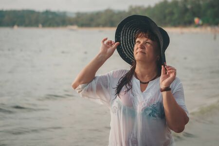 portrait of a tourist with long hair in black hat and a white t-shirt against the rocks and the sea. woman in travelの写真素材