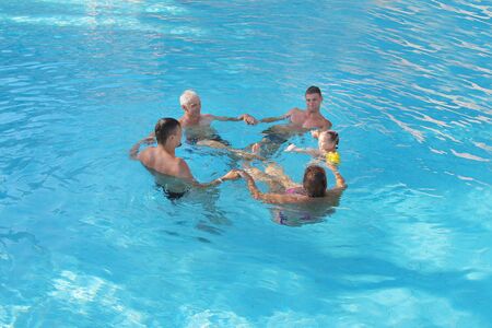The concept of sports, recreation, healthy lifestyle - 5 people swim in the pool forming a circle. People in the water holding handsの写真素材