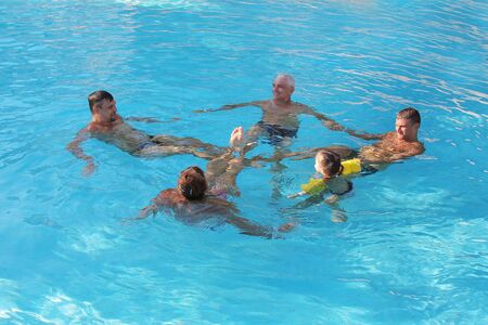 The concept of sports, recreation, healthy lifestyle - 5 people swim in the pool forming a circle. People in the water holding handsの写真素材