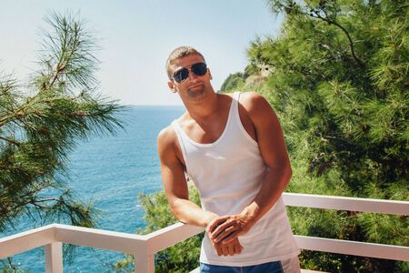 the concept of tourism, leisure is a beautiful man, basking in the white dress on the balcony of the hotel with views of tropical plants and seaの写真素材