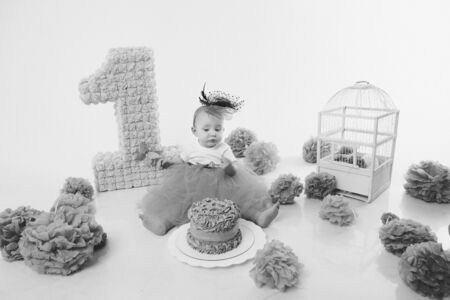 Birthday celebration: girl sitting on the floor among the numbers 1, artificial flowers and bird cageの写真素材