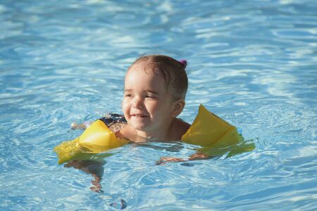 girl in armrests for swimming on vacation in the pool. The concept of Spa, swimming lessons, vacations, water treatmentの写真素材