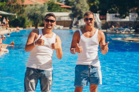 the concept of recreation, tourism - two smiling inflated men with glasses having fun by the poolの写真素材
