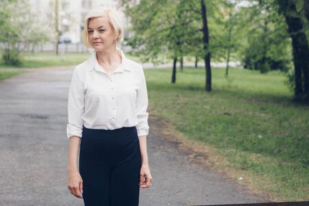 the concept of working on the street, day rest - a Fashionable stylish portrait of a woman with white short hair. businesswoman walking in the Park among the trees.の写真素材