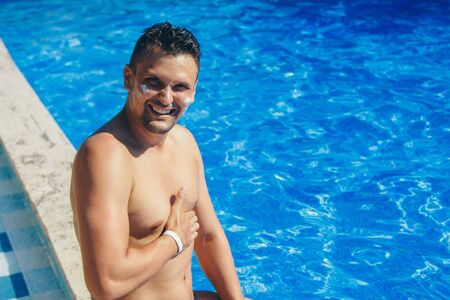 Portrait of a young tanned man with sunscreen on his face by the water. The concept of tanning, recreation, tourismの写真素材