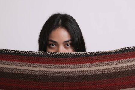 Asian girl covers her face with a handkerchief on white background. beautiful brunette with a stole in her face. The concept of religious life, Oriental beautyの写真素材