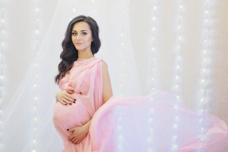 the pregnant woman in pink dress thought on white background. The concept of healthy digestion, lifestyle, IVFの写真素材