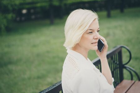entrepreneur talking on the phone in the Park. Blonde hair Bob works outside. businesswoman with smartphoneの写真素材