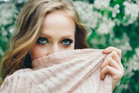 caucasian girl covers her face with a handkerchief on background of trees. beautiful blonde with blue eyes a stole in her face. The concept of religious life, Oriental beautyの写真素材