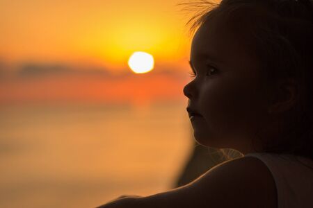 a little girl on the balcony overlooking the sea and the sunset. Silhouette against the sun. the concept of tourism, recreationの写真素材