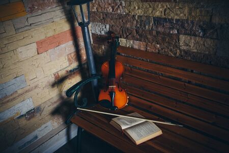 violin, bow and open book on a bench by the stone wallの写真素材