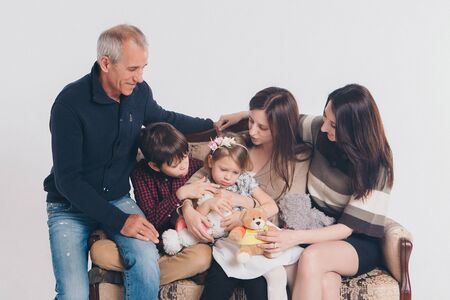 concept of happy childhood, family, love - group of people on a white background: adults and children with toys sitting on the same couchの写真素材