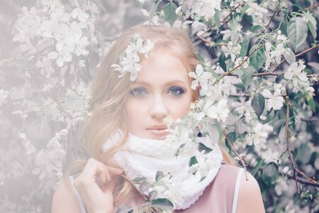beautiful blonde in a warm scarf among the flowers. Spring mood-a Woman with make-up of white flowersの写真素材