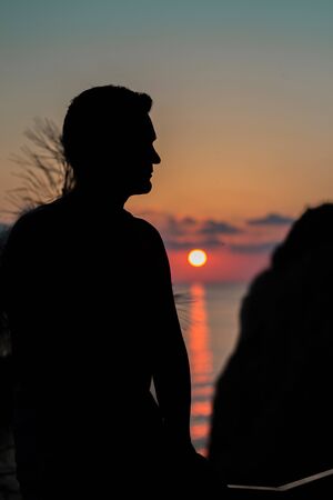 the concept of tourism, recreation-a happy man overlooking the sea and the sunset. silhouette of the peopleの写真素材
