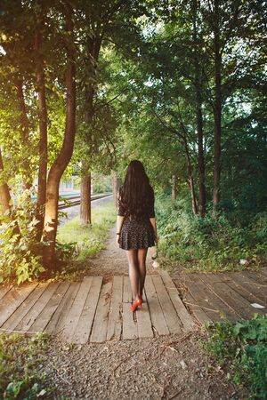 a beautiful brunette in a black dress and red shoes with a rose in her hands. Woman advertises accessories, clothes, shoesの写真素材