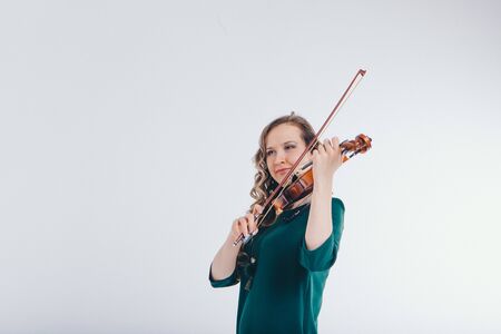 beautiful girl in green dress with small guitar in hands on white background. The concept of advertising musical instruments, fashion, symbolsの写真素材