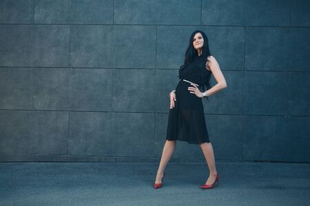 a beautiful brunette in a black dress and red shoes. Woman advertises accessories, clothes, shoesの写真素材