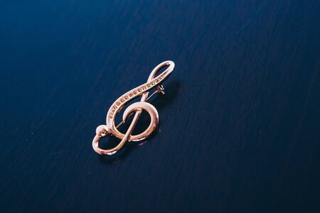 Gold violin on a dark background. embellishment: brooch. copy space. The concept of musical symbols, isolated objects, jewelry work, jewelryの写真素材