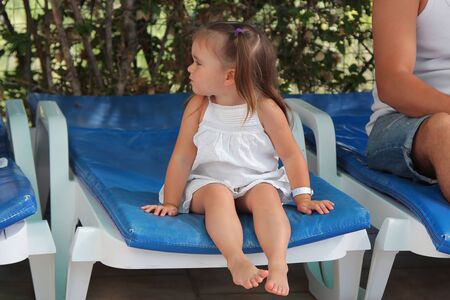 the concept of a days rest, relaxation, thoughtfulness, sunbathing, tan-the tanned girl rests sitting on a chair near the pool. Calm expression of face, relaxed postureの写真素材