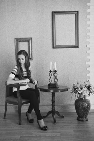 the girl is sitting at a table with candles, next to a vase of flowers and empty picture frames. Interior decoration concept, designの写真素材