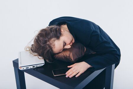 businesswoman in a business suit and with phone and laptop sleeping on the floor on a pillow on a white background. The concept of business everyday life, vacation, work breakの写真素材