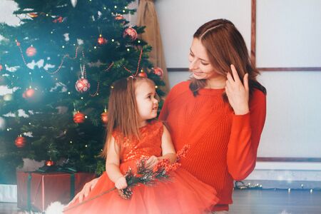 mother and daughter in red clothes unfold New year gifts under the Christmas tree. the concept of celebrating Christmas midnightの写真素材