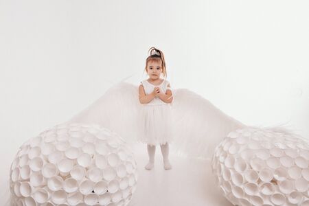 A girl in a white dress with angel wings holding on a white background. An angel-child have big white balls. The concept of Christmas, mystical creatures, Halloweenの写真素材