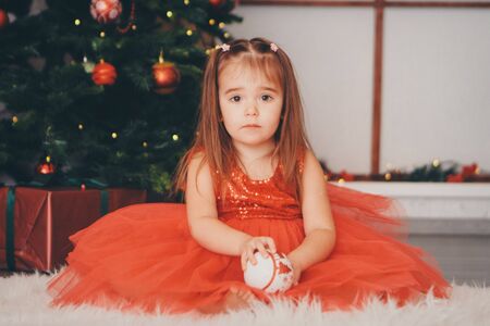 small girl in red clothes with snow ball in hand under the Christmas tree. the concept of celebrating Christmas ,midnight, new year,の写真素材