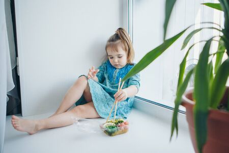 small child in traditional Chinese dress eating sushi sticks. girl in Japanese culture. concept of healthy food, Oriental cuisineの写真素材