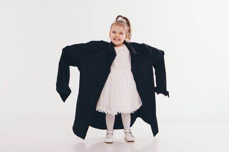 a little girl tries on dad's shirt. Child in big black clothes on white background. Concept of children's games, imitation of adult life, fashionの写真素材