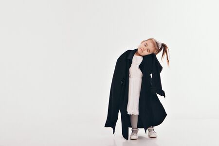 a little girl tries on dad's shirt. Child in big black clothes on white background. Concept of children's games, imitation of adult life, fashionの写真素材