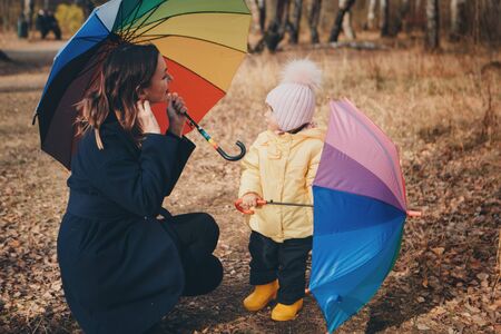 a small child with mother in a warm suit and with a colorful umbrella walks in the woods. autumn park. The concept of children's fashion, accessories, outdoor walksの写真素材